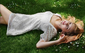 美麗的女孩躺在草地上，白色的禮服，姿勢