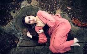 粉紅色連衣裙的女孩躺在樹樁